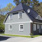 Ein graues Haus mit weißen Fenstern und einem dunklen Dach steht inmitten von Bäumen.