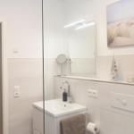 Badezimmer mit Spiegel, Waschbecken und Glaswand. Dekoration mit Bild und Pflanze.