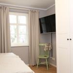 Schlafzimmer mit Bett, Fenster, TV und grüner Stuhl.