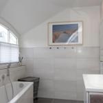 Badezimmer mit Badewanne, Waschbecken und Fenster mit Jalousien.