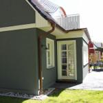 Ein Haus mit grauer Fassade, weißer Tür und Balkon. Außenbereich mit Tisch, Stühlen und Sonnenschirm.