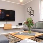 Wohnzimmer mit grauem Sofa, Holztisch und Wand-TV.