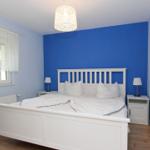 Schlafzimmer mit weißem Bett, blauer Wand und Nachttischen mit Lampen.