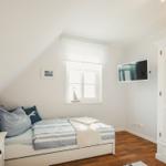 Schlafzimmer mit Bett, Nachttisch, TV und Kleiderschrank. Fenster mit Jalousie und Segelboot auf dem Fensterbrett.