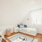 Schlafzimmer mit Dachschrägen, Bett, Nachttisch, Fenster und Teppich mit Ankergestaltung.
