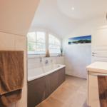 Badezimmer mit Badewanne, Fenster, Spiegel und Handtuchhalter.