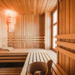 Holzsauna mit Sitzbänken und Fenster. Holzmulde und Wandlampe sichtbar.