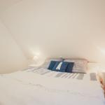 Schlafzimmer mit Bett, zwei Nachttischen und Lampen unter schrägen Wänden.