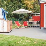 Terrasse mit Liegestühlen, Sonnenschirm und Grillplatz neben rotem Haus.