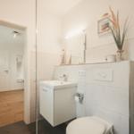 Badezimmer mit Waschbecken, Toilette und Dusche. Holzfußboden im Flur.