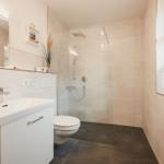 Badezimmer mit Dusche, Waschbecken und Toilette. Fenster und Heizkörper sichtbar.