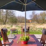Terrasse mit Tisch, Stühlen und Sonnenschirm. Hintergrund: Grasland und Bäume.