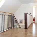 Haus mit Holzboden, Treppe und Dachfenster. Weiße Wände und Bilderrahmen.