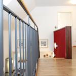 Treppenhaus mit grauem Geländer und rotem Schrank im Hintergrund.