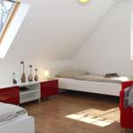 Zimmer mit Dachschrägen, zwei Betten, rotem Schrank und Fenster.