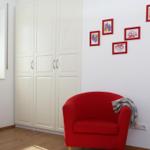 Ein Raum mit weißem Schrank, rotem Sessel und Bildern an der Wand.