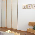 Schlafzimmer mit Kleiderschrank, Stuhl und Wandbildern.