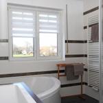 Badezimmer mit Badewanne, Dusche und Fenster mit Jalousie.