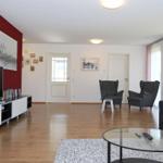 Wohnzimmer mit Holzboden, Sofa, zwei Sessel und Fernseher an roter Wand.