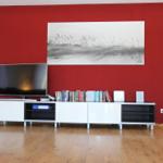 Roter Wandbereich mit Fernseher und Kunstwerk über einem weißen Sideboard.