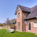 Rotes Backsteingebäude mit Terrasse, Liegestühlen und Satellitenschüssel. Grünflächen und Bäume im Hintergrund.