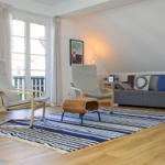 Wohnzimmer mit Sofa, zwei Sesseln und blau-weißem Teppich auf Holzboden.