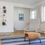 Wohnzimmer mit Bücherregal, Sessel und Fenster. Teppich und Kissen auf Holzboden.