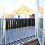 Terrasse mit schwarz-weißen Fliesen und Holzgeländer. Blick auf ein Haus mit gelbem Dach.