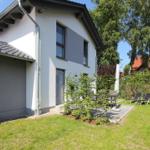 Moderne Villa mit Garten, Terrasse und Liegestühlen. Schwarze Fenster und graue Fassade.
