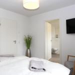 Schlafzimmer mit Bett, Fernseher und Sessel. Flur führt in die Toilette.