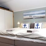 Schlafzimmer mit Doppelbett, Ankerkissen und Wandbild. Links Schrank, rechts Nachttisch mit Lampe.