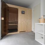 Sauna mit Holzverkleidung und Sitzbänken. Neben einem weißen Regal mit Holzschale.
