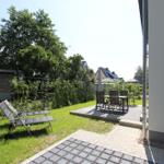 Hinterhof mit Liegestühlen und Tischset auf Terrasse. Grünfläche und Zaun sichtbar.
