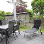 Terrasse mit Tisch, Stühlen und Liegestuhl. Hintergrund: Zaun und Haus.