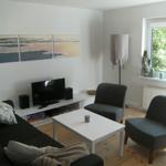 Wohnzimmer mit Sofa, zwei Sesseln, TV und Fenster mit Blick auf Garten.