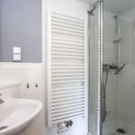 Badezimmer mit Dusche, Waschbecken und Heizkörper.