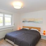 Schlafzimmer mit Doppelbett, Fenster und Wandbildern.