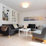 Wohnzimmer mit Sofa, Sessel, Couchtisch und Wandregalen. An der Wand hängen drei Bilder.