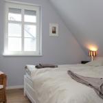 Schlafzimmer mit Dachschräge, Fenster und Bett. Neben dem Bett steht eine Lampe.