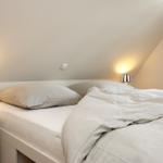 Schlafzimmer mit Bett, zwei Nachttischen und Lampen unter schrägem Dach