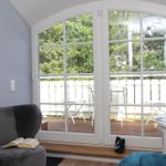 Ein Raum mit grauem Sessel, großem Fenster und Balkon mit Gartenblick.