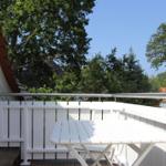 Terrasse mit weißem Tisch und Bänken, umgeben von Bäumen und einem klaren Himmel.