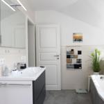Badezimmer mit Badewanne, Waschbecken und Dusche. Weiße Wände und graue Fliesen.