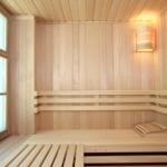 Holzsauna mit Sitzbänken und Fenster. Wandlampe an der Seite.