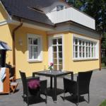 Außenbereich mit Tisch, Stühlen und Strandkorb vor gelbem Haus mit Balkon.
