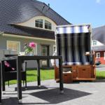 Terrasse mit Tisch, Stühlen und Strandkorb. Hintergrund: Haus mit Schieferdach.