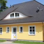 Ein gelbes Haus mit schwarzem Dach und weißen Fenstern. Vordere Tür mit Sonnenmotiv.