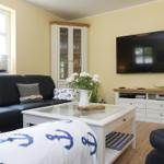 Wohnzimmer mit Sofa, Fernseher und Glaswand. Dekoration mit Ankern und Blumen.