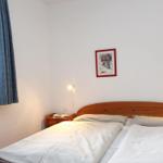 Ein Schlafzimmer mit Doppelbett, Holzkopfteil, Nachttisch und Fenster mit Vorhang.
