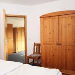Schlafzimmer mit Holzschrank, Stuhl und Blick in angrenzenden Raum.